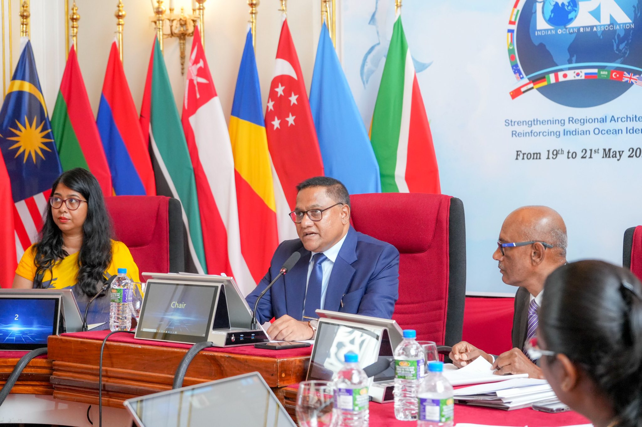 May be an image of 4 people, dais and text that says 'INDIAN OCEAN RDUSOCLONWEIMAIDOCIATON RIM ん ASSOCIATION Strengthening Regional StrengtheningRegionalArchit Archit Reinforcing Indian Ocean Ide From 19th to 21 May 20 Chair'