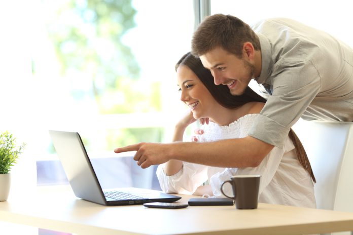 Side-view-of-a-happy-couple-searching-information-on-line-in-a-laptop-on-a-table-at-home-or-hotel-ro.jpeg